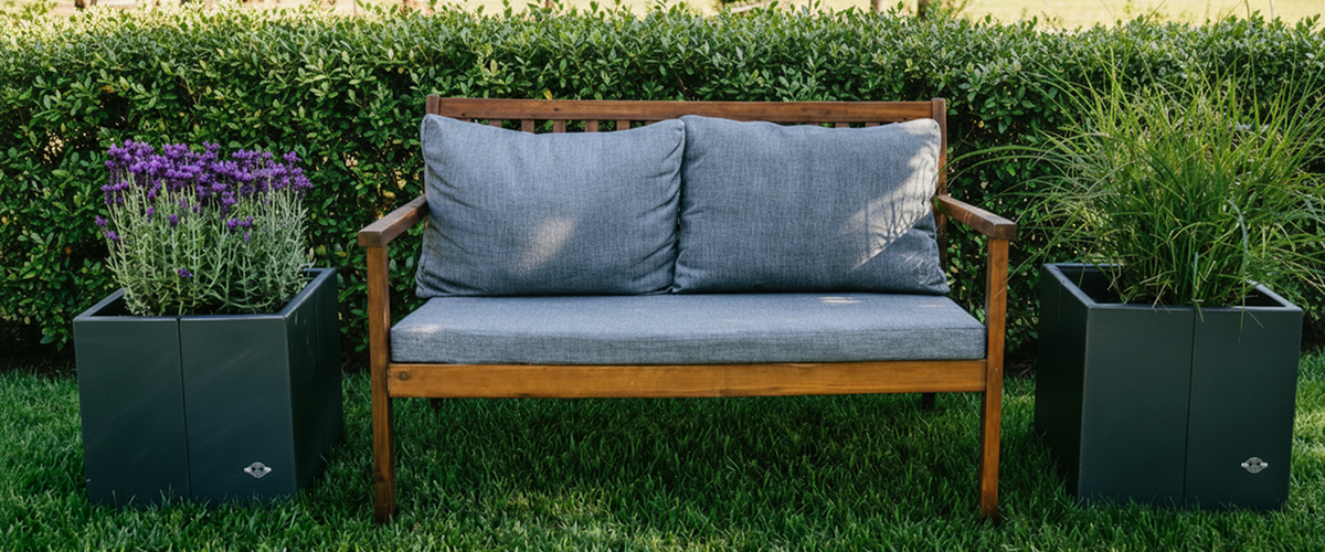 Metallpflanzkübel Vernazza in anthrazitgrau bepflanzt mit Gräsern und Lavendel neben einer Sitzbank im Garten.